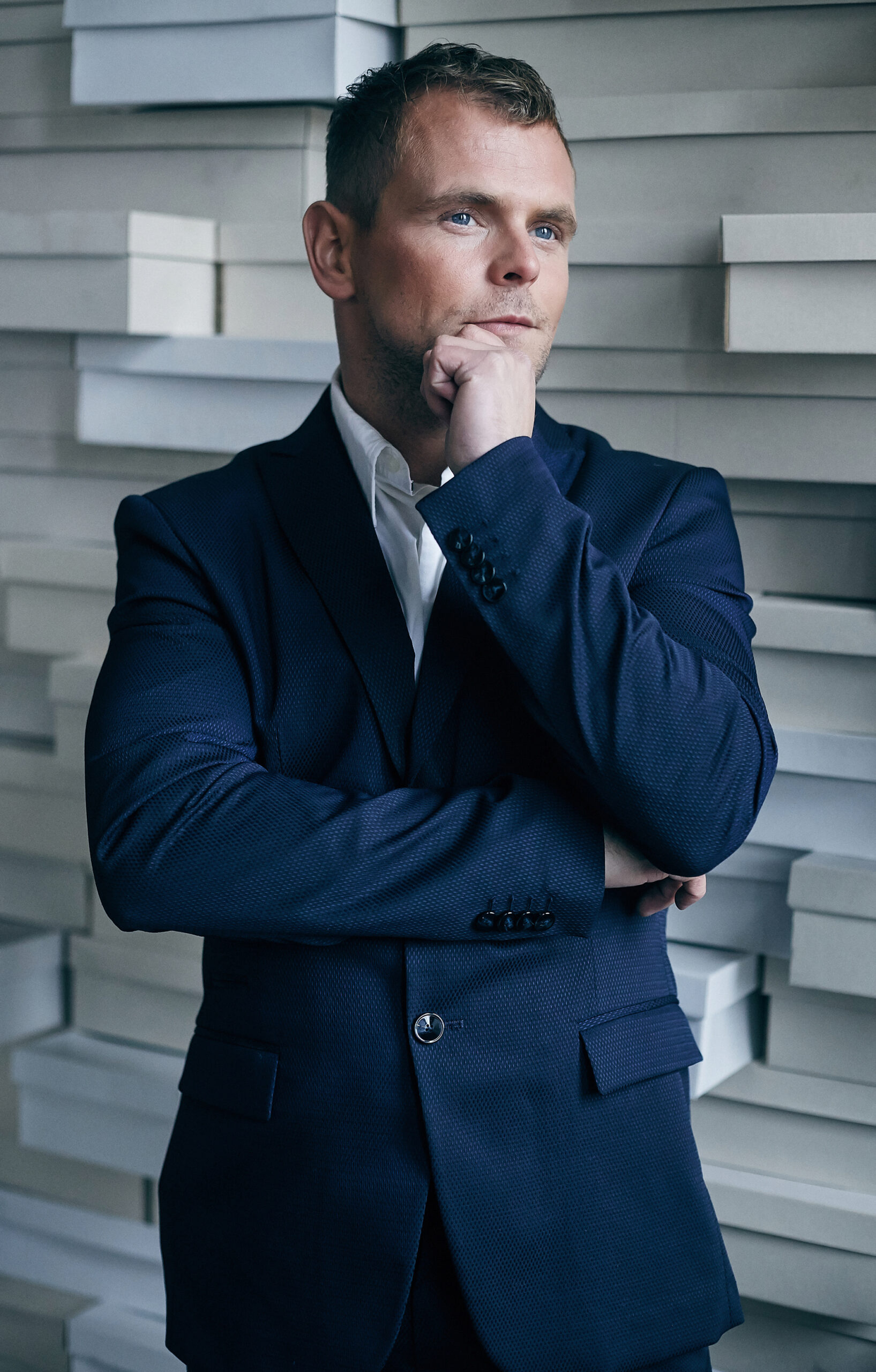 Man in blue suit posing over white artistic wall from bricks.